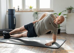 Mann macht in Wohnzimmer eine Eigengewichtsübung auf dem Boden. Durch das Fenster dringt helles Licht. Es stehen Functional Trainingsgeräte im Raum.